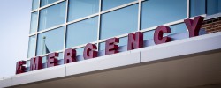 Emergency room entrance with red block letters on the metal awning of a hospital building, blue tone filter.